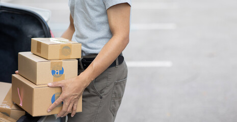 A delivery man is delivering cardboard boxes to customers at the door of a private car. young man delivery man in casual clothes Parcel moving service