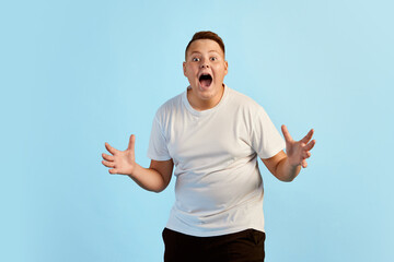 Success, wow. Excited teen boy, overweight model in white shirt shouting isolated over blue studio...