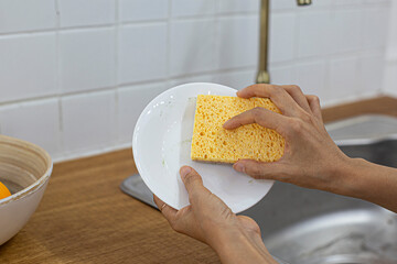 washing dishes plate with yellow sponge for dishes against the background of the sink.