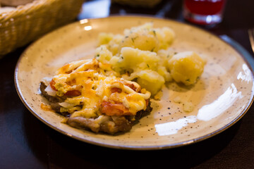 meat baked with cheese with boiled potatoes served on a plate in restaurant