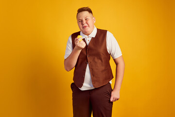 Cute boy in retro costume tasting lemon and expressing weird emotions isolated over orange color background. Vintage fashion, music, youth, emotions