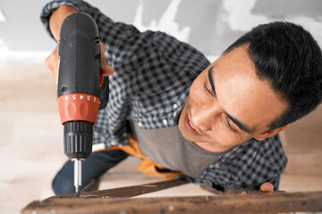 Overhead shot of young Asian man drilling into wood during home renovation