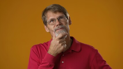 Fototapeta premium Portrait of thinking pondering mature man in red shirt having idea moment giving thumbs up on solid yellow studio background. Smiling happy guy showing eureka