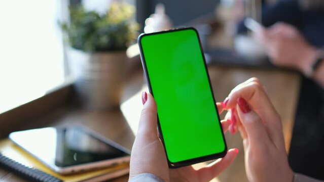 View from shoulder of caucasian woman doing swipe up gesture on chroma key of modern smartphone. Female relaxing in a Chinese restaurant and using cell phone.