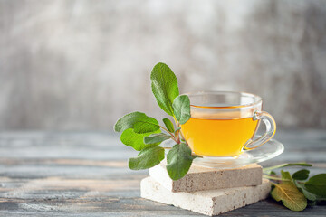 Sage herbal tea in a glass cup with fresh  leaves on wooden background. Natural medicine and...