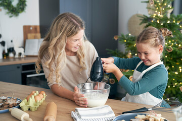 Caucasian mother and daughter preparing baking using electric mixer in the kitchen before Christmas