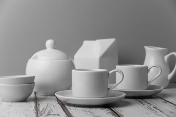 a set of white ceramic tableware on a light background. Various types of white plates, bowls and platters, cups, saucers, milkmen. Simple white tableware for use at home or in a cafe.