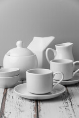 a set of white ceramic tableware on a light background. Various types of white plates, bowls and platters, cups, saucers, milkmen. Simple white tableware for use at home or in a cafe.