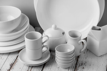 a set of white ceramic tableware on a light background. Various types of white plates, bowls and platters, cups, saucers, milkmen. Simple white tableware for use at home or in a cafe.