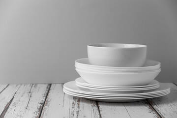 a set of white ceramic tableware on a light background. Various types of white plates, bowls and platters, cups, saucers, milkmen. Simple white tableware for use at home or in a cafe.