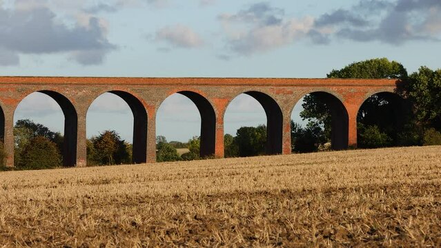 Red brick viaduct in a field amongst a cloudy sky