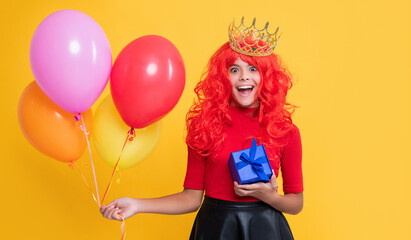 happy child in crown with gift box and party balloon on yellow background. wow