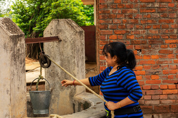 A beautiful young solo tourist bulling a bucket of water from well for drinking. Concept of save...