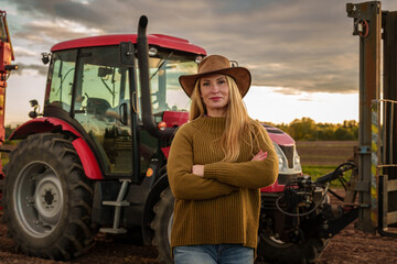 Portrait of confident farmer woman and modern combine on cultivated field.