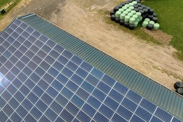 Aerial view of blue photovoltaic solar panels mounted on farm building roof for producing clean...