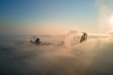 Aerial view of cement factory with high concrete plant structure and tower crane at industrial manufacturing site on foggy evening. Production and global industry concept