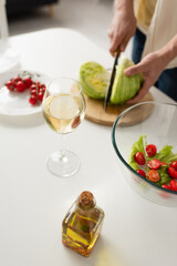 partial view of blurred man cutting lettuce near bowl with vegetable salad and glass of white wine.