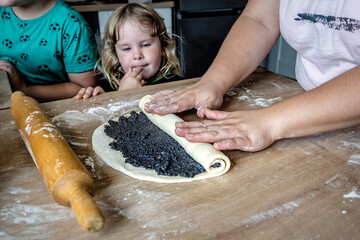 Mother makes a poppy seed roll while the child watches