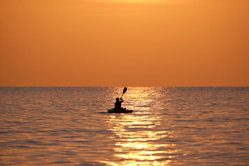 Fototapeta premium Dark silhouette of lonely fisherman rowing on his boat on sea water at sunset