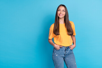 Portrait of pretty gorgeous cute girl long hairdo wear yellow t-shirt look empty space arms in pockets isolated on blue color background
