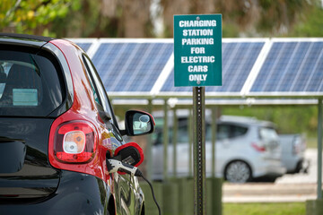 Electric plug-in car charging with electricity from solar renewable power source parked on city...