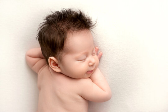 Top view of a newborn baby girl lying without clothes on a white bed. Beautiful portrait, naked back of a little sleeping girl with closed eyes 7 days, one week. Photography in macro studio.