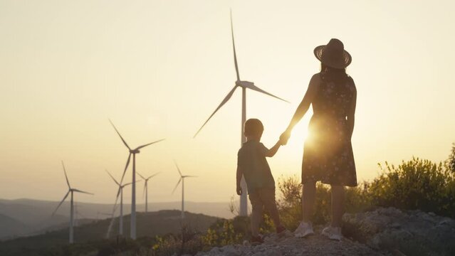 Lifestyle video of a mother with her son on a walk near the windmills. Wind power plant at sunset, people study renewable clean energy. High quality 4k footage