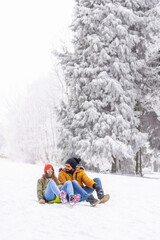 Couple having fun sliding down the hill in the snow while on winter vacation