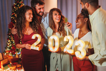 Friends holding illuminative numbers 2023 at New Years Eve midnight countdown