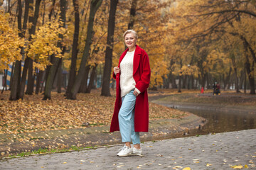 Portrait of a beautiful middle-aged woman in a red coat, autumn park