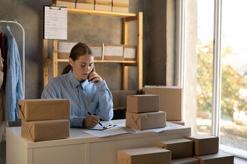 Small business owners, startup and e-commerce concept. Smiling friendly young woman talking with customer over phone, while packing orders for shipping, online clothes store