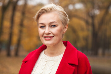 Portrait of a beautiful middle-aged woman in a red coat, autumn park