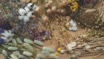 A colorful close up of dried flowers, fragrant herb leaves, and seed pods lays on the wooden table. Materials for making herbarium. Autumn background.