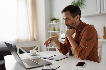 Fototapeta premium pensive man thinking near empty notebook and gadgets in kitchen.