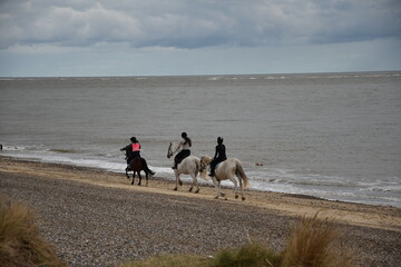 Obraz na płótnie Canvas People horse riding on the beach with a cloudy sky background. Taken in Lowestoft England. 