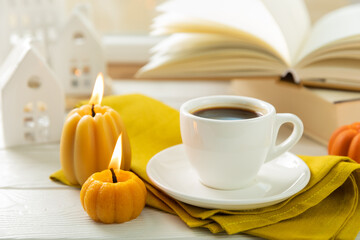 Autumn composition, a cup of hot coffee, a decorative little house, pumpkin candles, books and a warm sweater on a wooden table. Seasonal morning hot coffee. Cozy interior decor