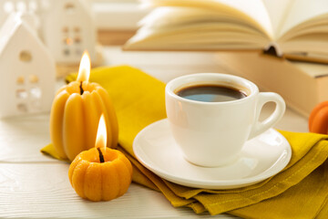 Fototapeta na wymiar Autumn composition, a cup of hot coffee, a decorative little house, pumpkin candles, books and a warm sweater on a wooden table. Seasonal morning hot coffee. Cozy interior decor