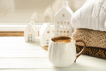 Winter.Winter composition, a cup of hot coffee, a decorative small snow-covered house and a warm sweater on a wooden table.Seasonal morning hot coffee.Merry Christmas and Happy New Year!Cozy interior