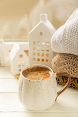 Winter.Winter composition, a cup of hot coffee, a decorative small snow-covered house and a warm sweater on a wooden table.Seasonal morning hot coffee.Merry Christmas and Happy New Year!Cozy interior