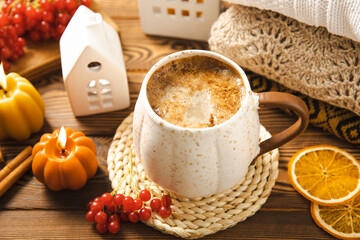 Autumn composition, a cup of hot coffee, a decorative little house, pumpkin candles, books and a warm sweater on a wooden table. Seasonal morning hot coffee. Cozy interior decor