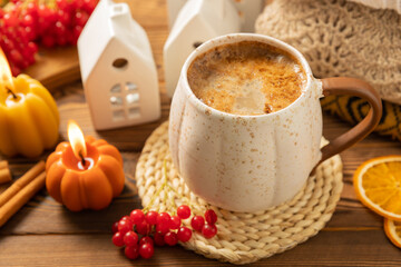 Autumn composition, a cup of hot coffee, a decorative little house, pumpkin candles, books and a warm sweater on a wooden table. Seasonal morning hot coffee. Cozy interior decor