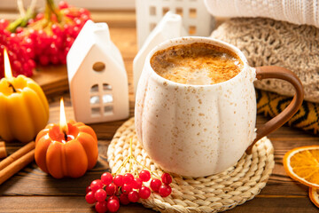 Autumn composition, a cup of hot coffee, a decorative little house, pumpkin candles, books and a warm sweater on a wooden table. Seasonal morning hot coffee. Cozy interior decor
