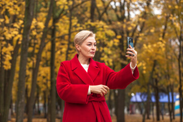 Portrait of a beautiful middle-aged woman in a red coat, autumn park