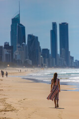 beautiful long-haired girl in long colorful dress walks along beach in gold coast on sunny day; beach with huge skyscrapers; miami beach in gold coast, australia