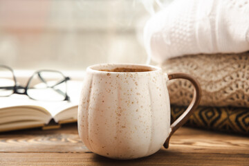 Fototapeta na wymiar Autumn composition, a cup of hot coffee, a decorative little house, pumpkin candles, books and a warm sweater on a wooden table. Seasonal morning hot coffee. Cozy interior decor