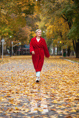 Fototapeta premium Portrait of a beautiful middle-aged woman in a red coat, autumn park