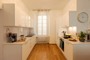 Modern white kitchen with parquet. On the fire there is the pot with the pasta and the hood light is on.