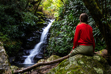 beautiful girl sits under a tropical waterfall in lamington national park, near gold coast in...