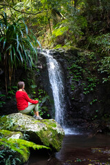 Fototapeta na wymiar beautiful girl sits under a tropical waterfall in lamington national park, near gold coast in queensland, australia; waterfall in tropical rainforest in australia, rainforest walk