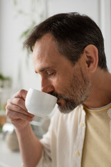 portrait of man with grey beard enjoying morning coffee on blurred background.